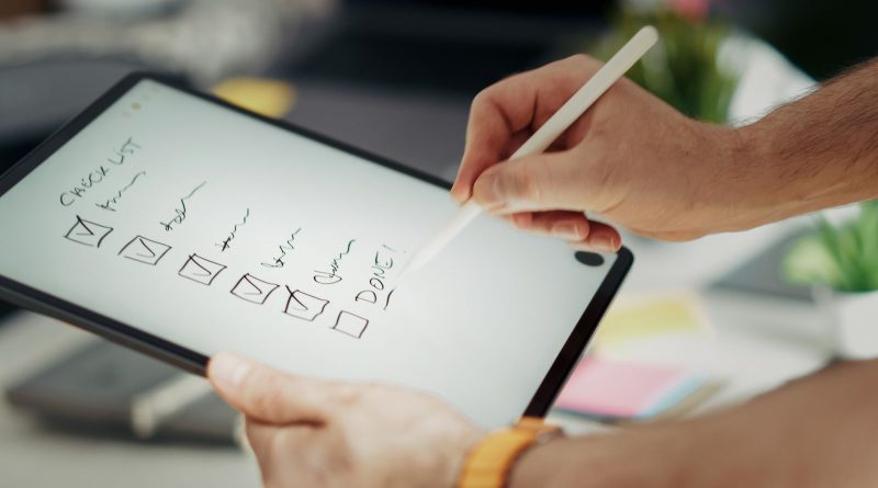 Close-up of a hand writing on a digital checklist using a stylus on a tablet, enhancing productivity.